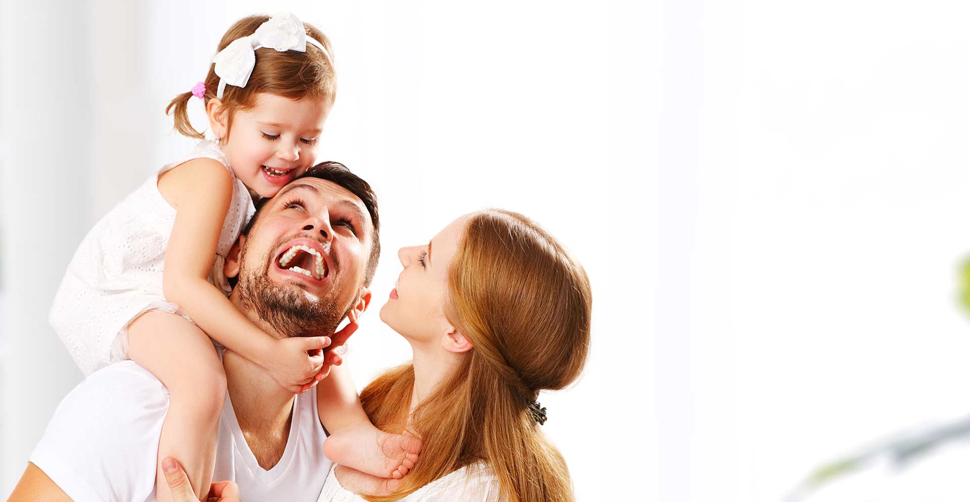 A little girl sitting on top her dad's shoulder and the mother smiling at them